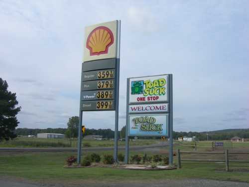 Gas station sign displaying fuel prices and a welcome sign for Toad Suck, Arkansas.