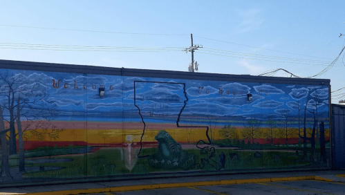 Mural depicting Louisiana landscape with trees, clouds, and a welcome message. Bright colors and scenic view.