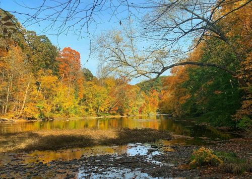A serene river scene surrounded by vibrant autumn foliage and clear blue skies.