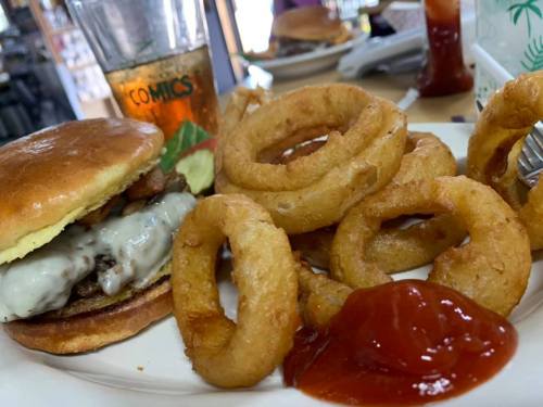A juicy burger with melted cheese and bacon, served with crispy onion rings and ketchup on a plate.