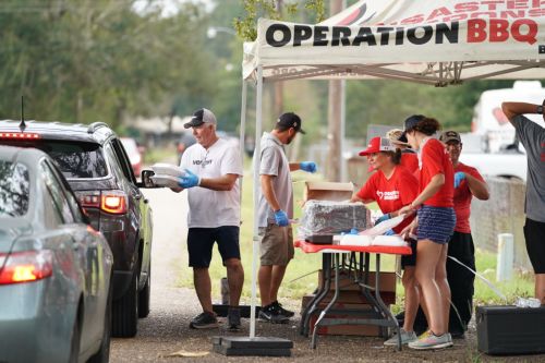 Volunteers serve food from a tent to cars in a community event, promoting support and assistance.
