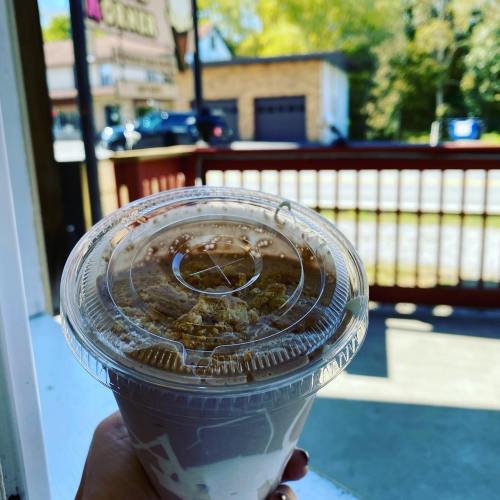 A hand holding a clear cup filled with a layered dessert, featuring a creamy top and a sprinkle of granola.