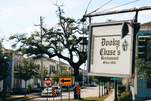 Sign for Dooky Chase's Restaurant, established in 1941, with a tree and street signs in the background.