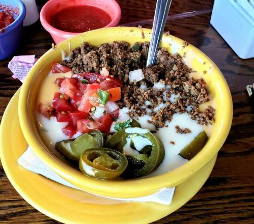 A yellow bowl filled with creamy white dip, topped with ground meat, diced tomatoes, onions, and jalapeños.