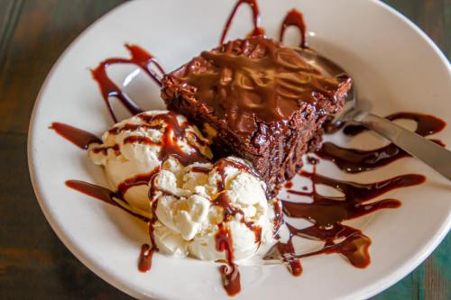 A plate with a brownie topped with chocolate sauce, served alongside two scoops of vanilla ice cream.