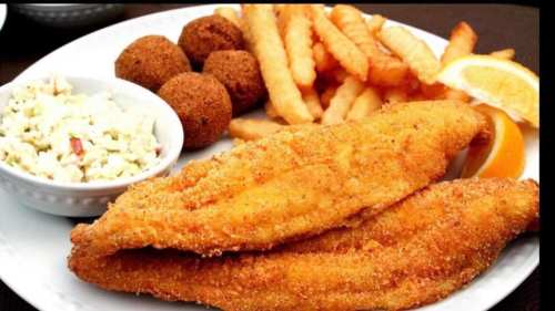 A plate of fried fish fillets, crinkle-cut fries, hushpuppies, coleslaw, and lemon wedges.