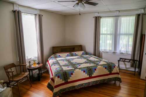 Cozy bedroom with a large quilted bed, wooden furniture, and natural light from two windows.