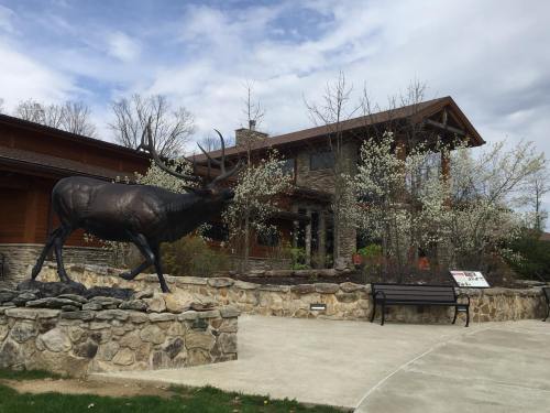 A large moose statue stands in front of a wooden building surrounded by flowering trees and a stone wall.