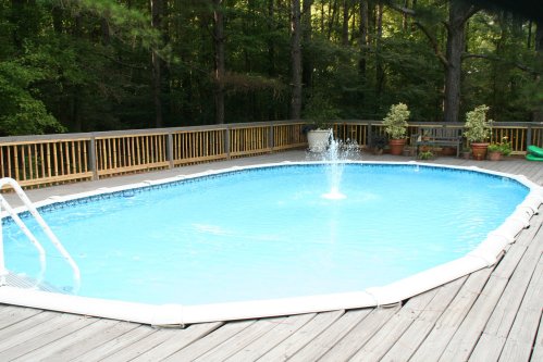 A serene outdoor pool surrounded by a wooden deck and potted plants, set in a lush, green forest.