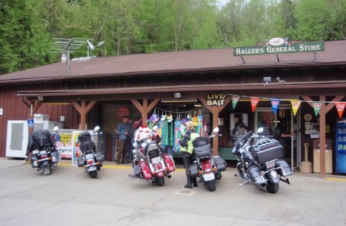 A row of motorcycles parked outside Haller's General Store, surrounded by greenery and colorful banners.