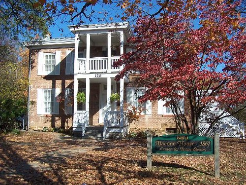 Historic brick house with white columns, surrounded by autumn leaves and a sign reading "Bacone House 1867."