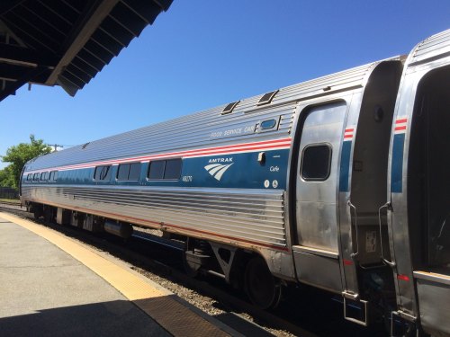Amtrak train car at a station, featuring a silver exterior with blue and red accents under a clear blue sky.