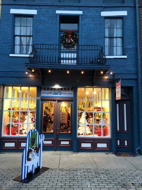 A festive storefront with holiday decorations, featuring a wreath and colorful displays in the windows.
