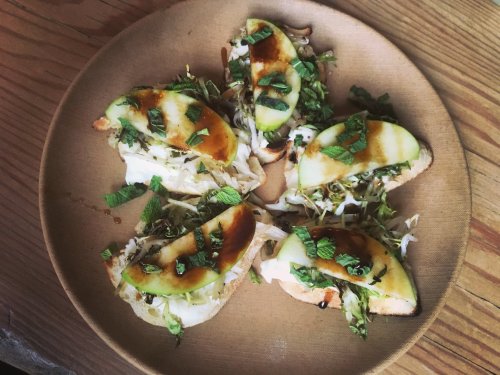 A plate of open-faced sandwiches topped with cabbage, green apple slices, mint, and a drizzle of sauce.