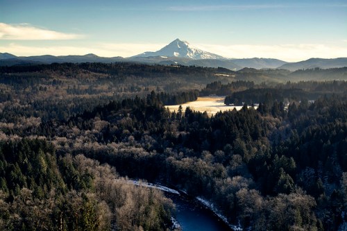 A panoramic view of a mountainous landscape with a snow-capped peak, lush forests, and a winding river below.