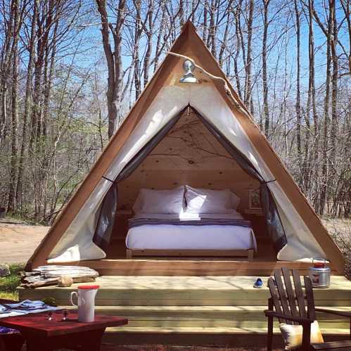 A cozy glamping tent with a bed, set in a wooded area, surrounded by nature and outdoor seating.