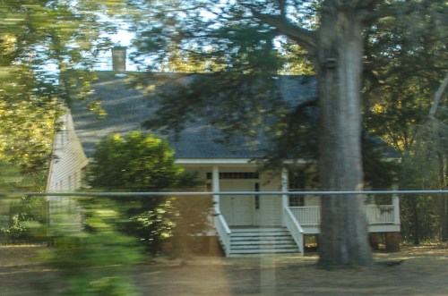 A blurred image of a two-story house surrounded by trees, with a front porch and steps leading to the entrance.