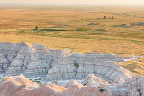 A panoramic view of layered rock formations in a vast, grassy landscape under soft sunlight.