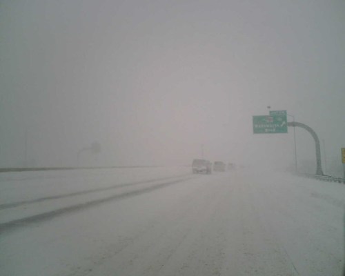 A snowy highway scene with low visibility, cars driving cautiously in a winter storm.