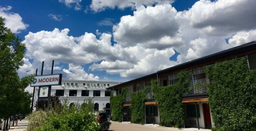 A modern building with greenery, under a bright blue sky filled with fluffy clouds.