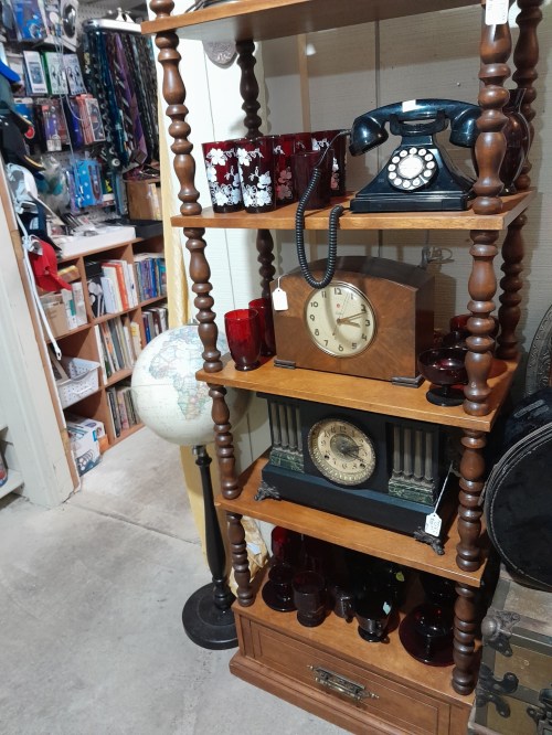 A wooden shelf displays vintage items: red glasses, an old telephone, a clock, and a globe, in a cozy shop setting.