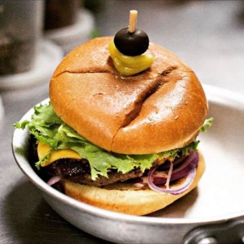 A delicious burger with lettuce, cheese, onions, and a pickle on top, served in a metal dish.