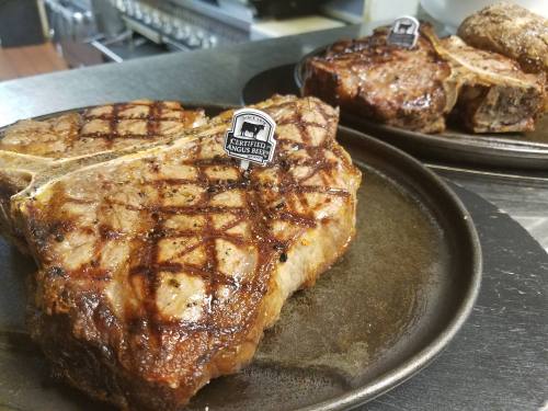 Two grilled T-bone steaks on metal plates, showcasing a charred crosshatch pattern and branded tags.