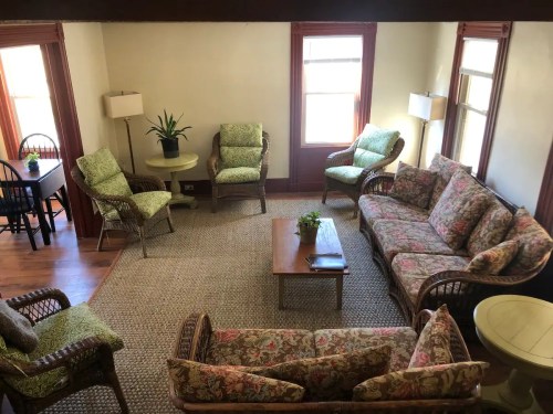 Cozy living room with floral-patterned furniture, a coffee table, and natural light from windows.