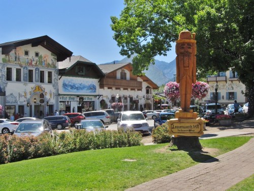 A sunny street scene in Leavenworth, WA, featuring a wooden statue and charming Bavarian-style buildings.