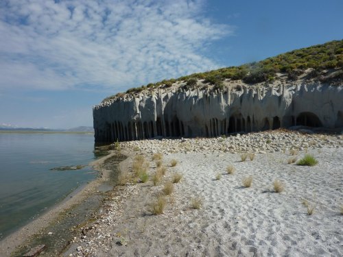 A sandy shore with rocky cliffs and gentle waves under a blue sky with scattered clouds.
