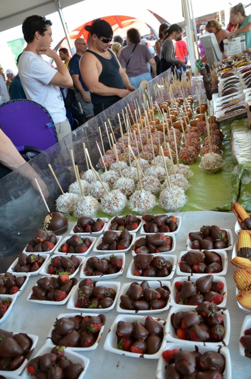 A vibrant market stall displays chocolate-covered strawberries and various decorated cake pops on sticks.