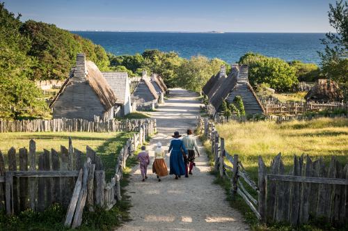 A scenic view of a historic village with thatched-roof houses, a dirt path, and people walking towards the ocean.