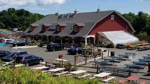 A red barn-style building with a greenhouse, surrounded by parked cars and outdoor seating in a garden center.