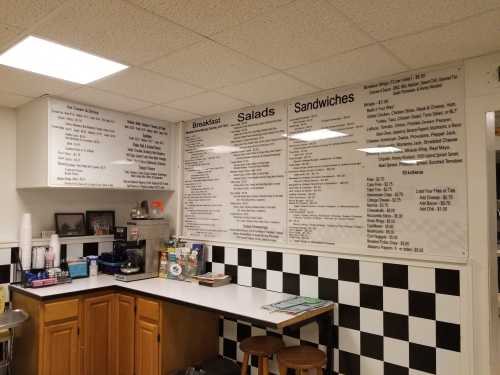 A cafe menu displayed on the wall, featuring breakfast, salads, and sandwiches, with a checkered floor and countertop.