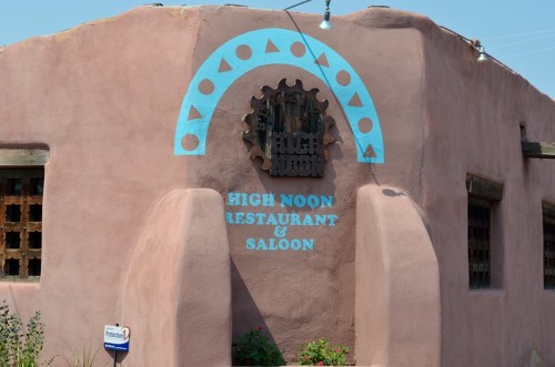 Exterior of High Noon Restaurant & Saloon, featuring a pink adobe wall and decorative blue arch above the entrance.