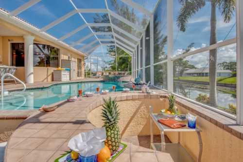 A sunny pool area with a screened enclosure, featuring a pool, tropical decor, and a view of palm trees.