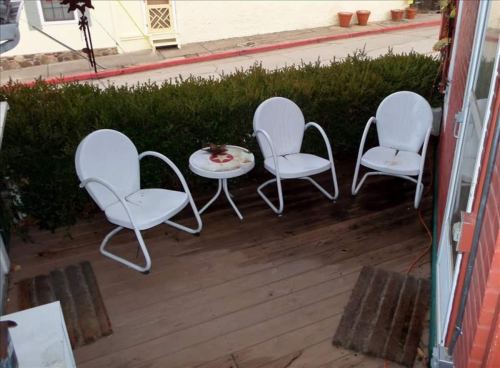 A small outdoor seating area with three white chairs and a round table, surrounded by greenery.