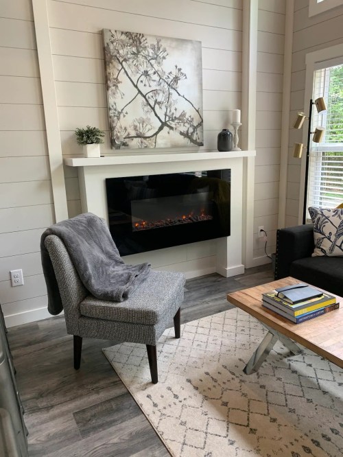 Cozy living room with a modern electric fireplace, a gray chair, a coffee table, and a decorative wall art.