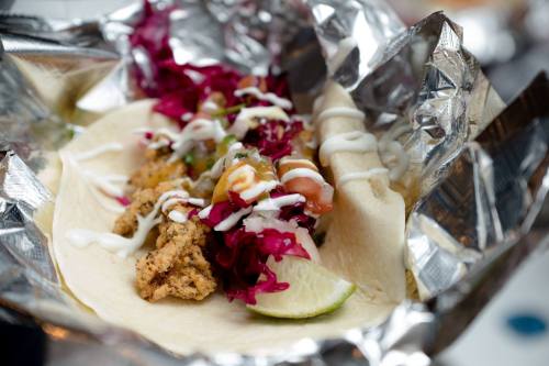 A taco filled with fried fish, colorful slaw, salsa, and a lime wedge, wrapped in foil.