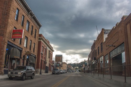 A quiet street in a historic town, lined with brick buildings under a cloudy sky.