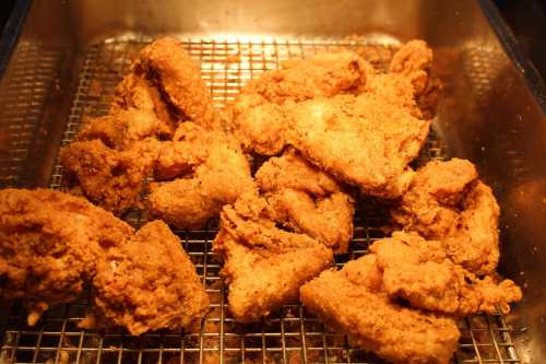 A close-up of crispy, golden-brown fried chicken pieces in a metal tray.