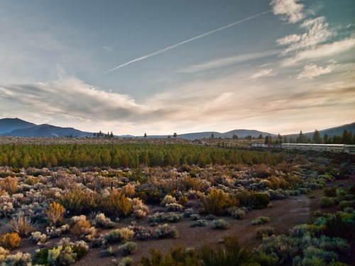A scenic landscape featuring rolling hills, sparse vegetation, and a cloudy sky at dusk.