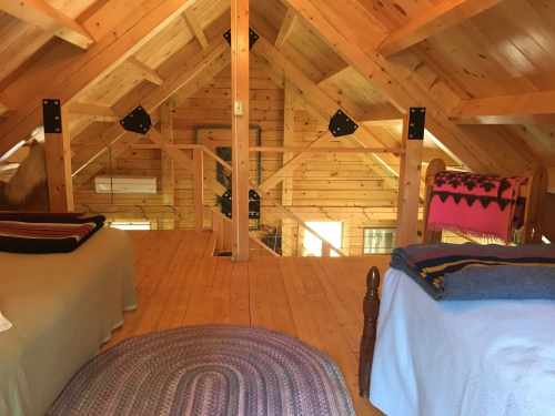 Cozy wooden loft with two beds, a woven rug, and warm, natural light from the windows.
