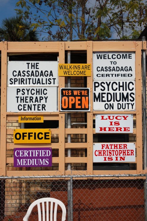 A wooden signboard displaying various signs for a psychic therapy center, including "OPEN" and names of mediums.