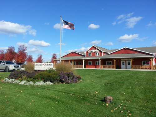 A red barn-style building with a flag, surrounded by green grass and colorful flowers under a blue sky.