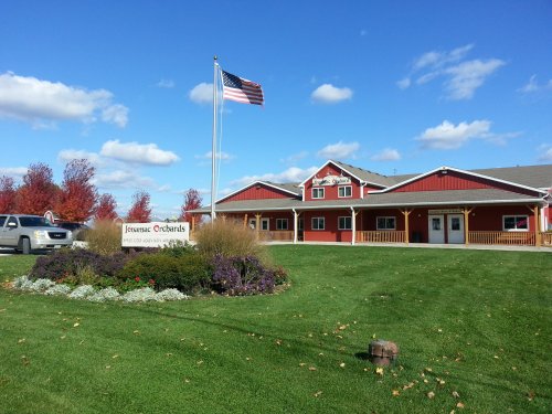 A red barn-style building with a flag, surrounded by green grass and colorful flowers under a blue sky.