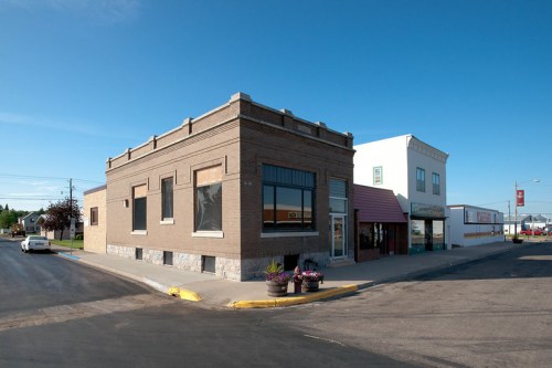 A brick building on a street corner, featuring large windows and planters, with a clear blue sky above.