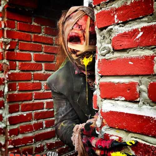 A creepy figure with a distorted face peeks from behind a brick wall, covered in yellow paint and wearing tattered clothing.