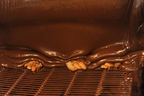 A close-up of flowing chocolate with nuts partially submerged in a smooth, glossy surface.