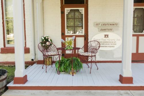 A cozy porch with two red chairs, a small table, and potted plants, inviting relaxation at a historic inn.